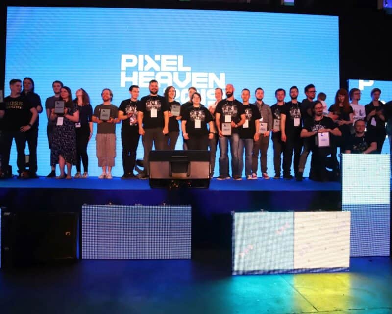 ogłoszono nominacje, na grafice widzimy ludzi stojących na scenie, za ich plecami jest ekran z wielkim logiem Pixel Awards Europe 2021