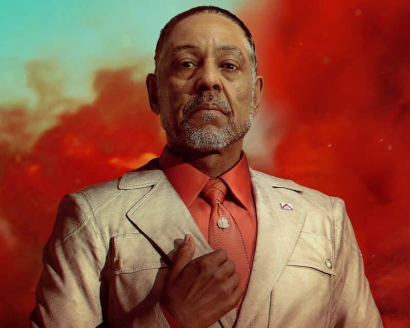 na obrazku El Presidente, antagonista gry Far Cry 6, który w liście do graczy wyśmiewa ich, w tle za nim czerwony dym, mężczyzna stoi w białym garniturze