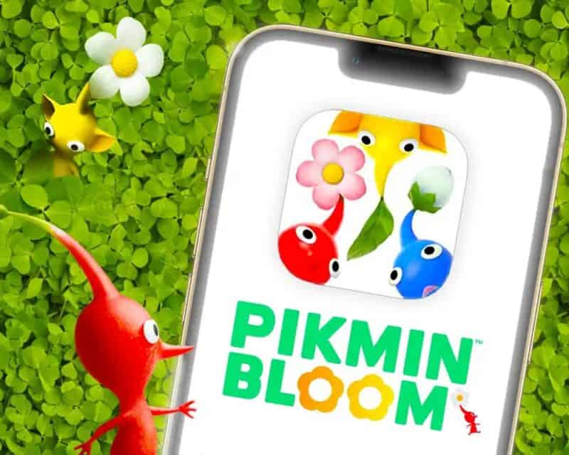 na grafice widać telefon z grafiką pikmin, na której jest napis z tytułem gry w kolorze zielonym i dwa kolorowe stworki w okienku, w tle łąka z trawą i kwiatami, post przedstawia bloom zwiastun premierowy
