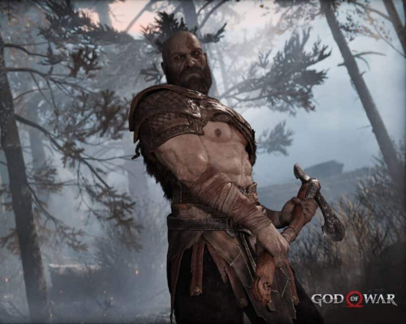 Kratos z gry God of War stoi z gołą klatą, jak zwykle!, z toporem w rękach, przodem do widza, w oddali drzewa i mgła, post przedstawia wymagania sprzętowe do gry