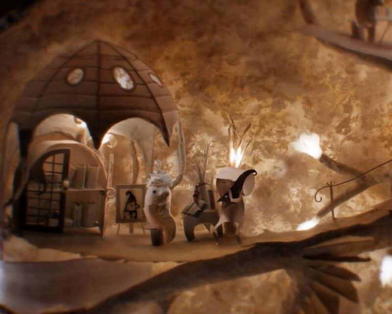 screen z gry Papetura, papierowe ludziki siedzące przed domkiem z papieru obok schodów z papieru, Papetura paszporty polityki