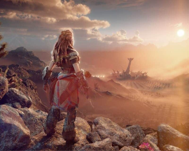 Młoda dziewczyna z rudymi włosami stoi tyłem do widza z przodu obrazka, patrzy w dal na ciągnącą się po horyzont pustynię z tajemniczą budowlą w oddali, może wypatruje kontynuacji Horizon Forbidden West