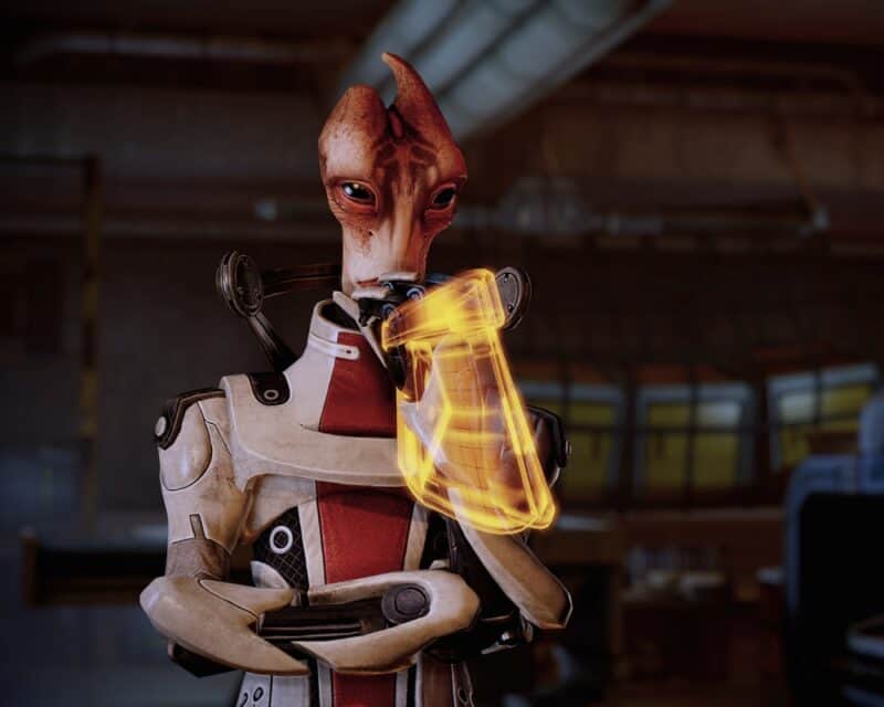 Mass Effect 2: Legendary Edition – istota humanoidalna (Salarianin) o podłużnej, czerwonawej twarzy ze skośnymi, czarnymi oczami, w biało-czerwonym kombinezonie i z pomarańczowym holo urządzeniem na ręce, Mass Effect 2 nieoficjalny patch