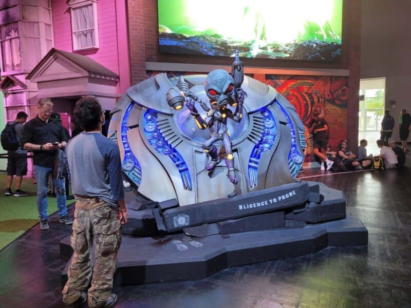 zdjęcie przedstawia statek kosmiczny i obcego z czerwonymi oczami i pistoletami, na dole dekoracji napis "#licencetoprobe". Obok dekoracji stoi mężczyzna (tyłem do kamery) i patrzy się na nią