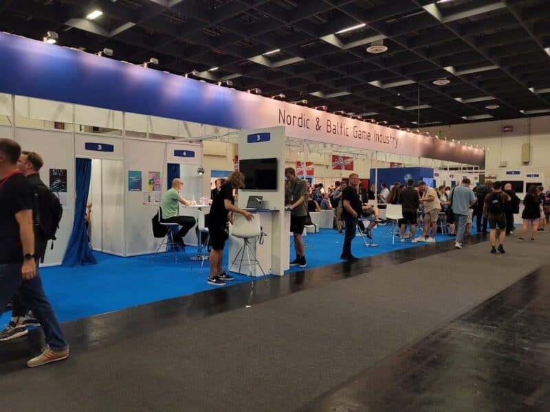 zdjęcie przedstawia wspólne stoisko studiów nordyckich i bałtyckich, jest utrzymane w bieli i niebieskich kolorach, widać dużo ludzi i stoiska do grania
