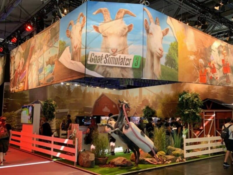 zdjęcie pochodzi ze strony jaxon.gg i przedstawia fragment dekoracji dla gry Goat Simulator 3, widać na nim kozę z długim językiem i podłączonym jetpackiem, w tle widać także stodołę i białe płotki, relacja gamescom 2022