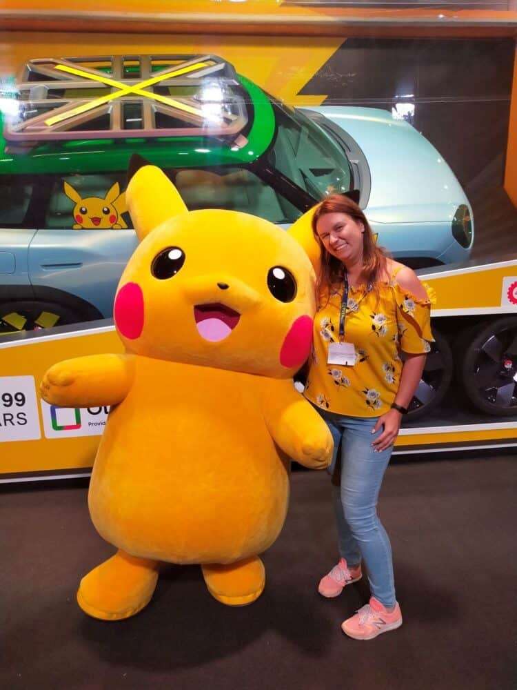zdjęcie przedstawia kobietę w żółtej koszulce w kwiaty, niebieskich jeansach i ludzkich rozmiarów maskotkę Pikachu, pozują razem do zdjęcia. w tłe widać zapakowany, również rzeczywistych rozmiarów, model Cooper Mini w kolaboracji z Pokemonami