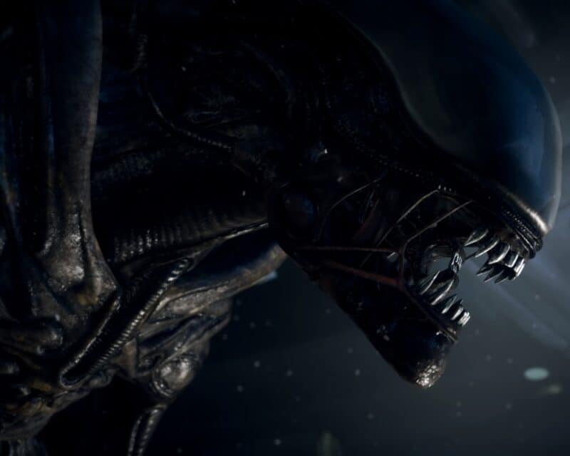 grafika z gry Alien: Isolation, przedstawia Ksenomorfa z profilu, jak stoi i nasłuchuje czegoś w okolicy, przez lekko rozchylone szczęki widać jego charakterystyczny mały język, również zakończony zębami, alien isolation kontynuacja nowa gra