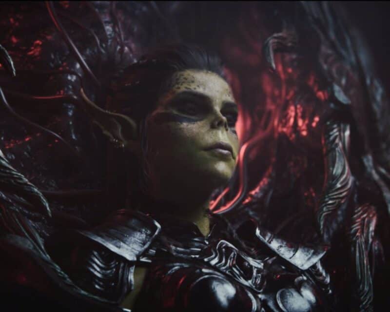 postać o zielonkawej skórze siedzi w dziwnym żelaznym lub kościstym tronie, krześle lub zamknięciu, śpi, screen z intra Baldur's Gate 3