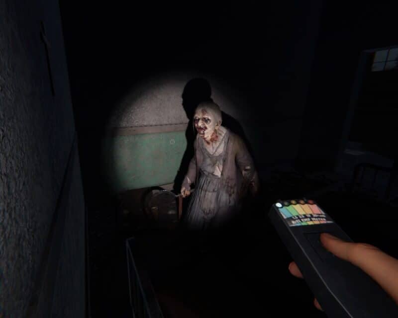 Phasmophobia wchodzi na konsole – screen z gry, EMF w ręce graczki (FPP), punktowe światło latarki oświetla ducha