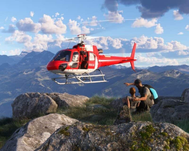 scenka w górach, widzimy dwie postaci czekające na szczycie góry lub łące górskiej, do których właśnie podlatuje czerwony helikopter ratunkowy