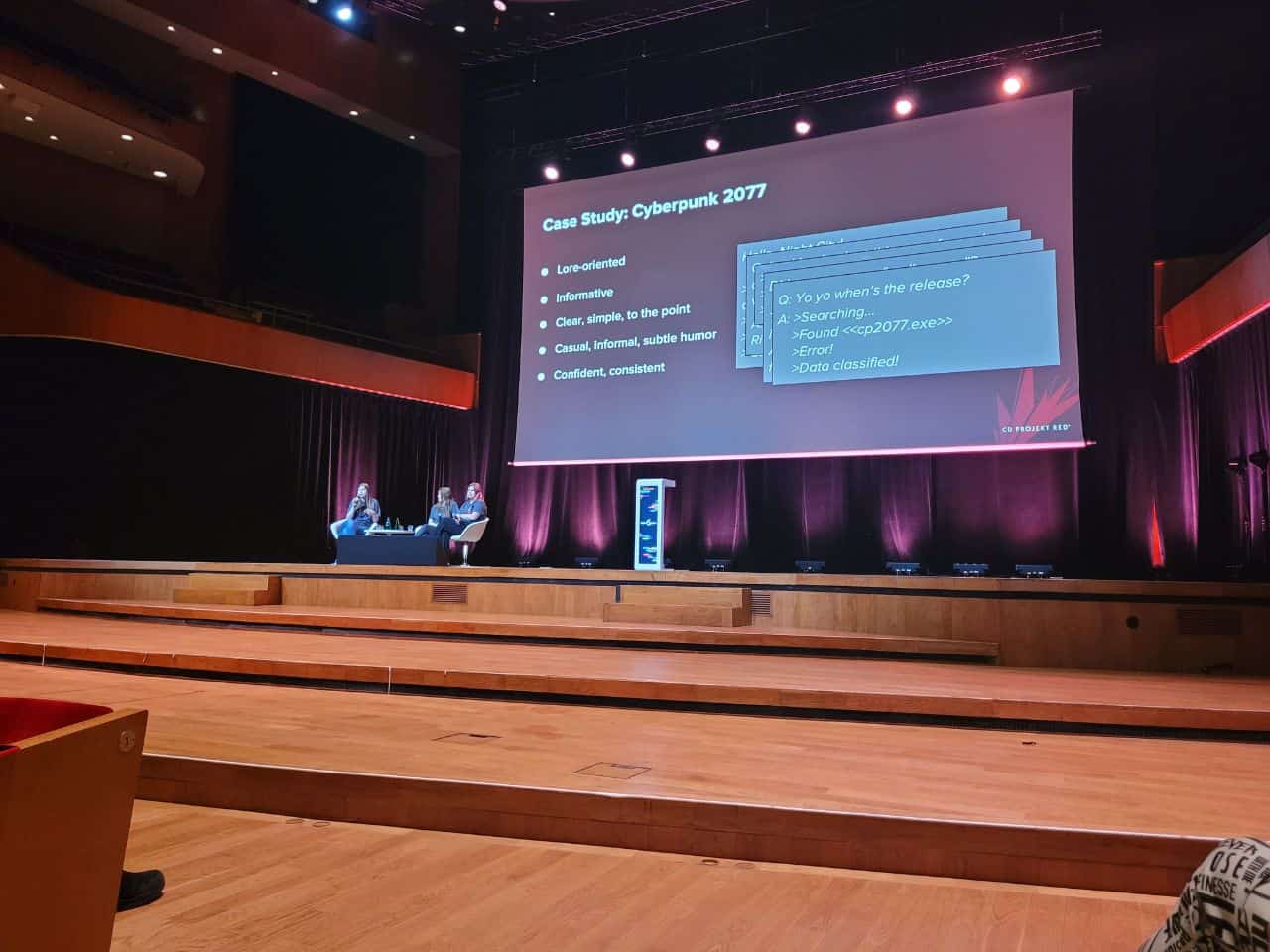 Digital Dragons 2023, wykład o community managemencie od CD Projekt RED, widzimy dużą scenę i schodki na nią, na scenie siedzą trzy kobiety, za nimi wielki ekran i prezentacja