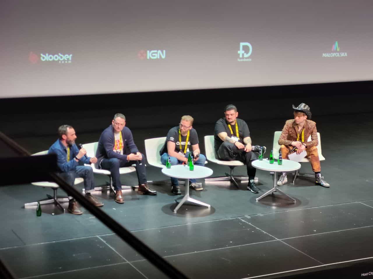 Digital Dragons 2023, panel o horrorach, pięciu mężczyzn siedzi jeden obok drugiego na osobnych krzesłach i rozmawia o grach