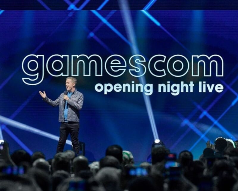 Gamescom Open Night Live pokaz, na scenie stoi prowadzący mężczyzna, za nim wielki ekran z nazwą wydarzenia, na dole widać głowy publiczności