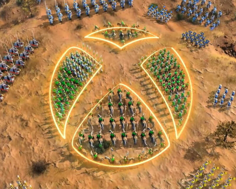 Obrazek przedstawia pole walki, na którym znajdują się różne jednostki wojsk. W centrum grafiki jest logo Xboksa.