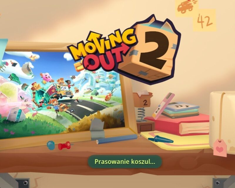 Moving Out 2 – ekran otwierający grę. Grafika przedstawia biurko ze zdjęciem w ramce, książką, kubkiem i dyskietkami.