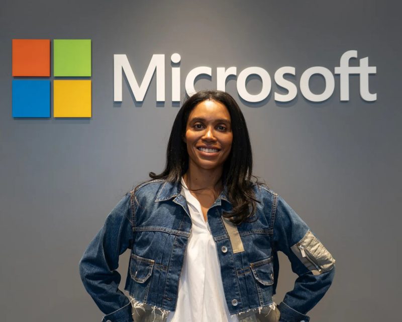 Nowa szefowa Xboksa, Sarah Bond, stoi na tle ściany z logiem Microsoftu.