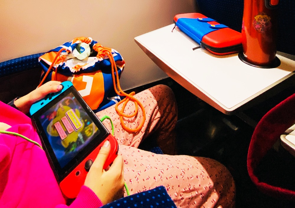 Dziecko grające na konsoli Nintendo Switch w trakcie podróży pociągiem.