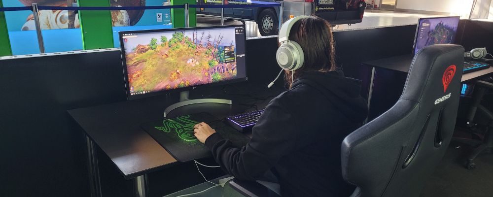 PGA 2022: na pierwszym planie dziewczyna siedząca przed monitorem w wygodnym krześle komputerowym Genesis