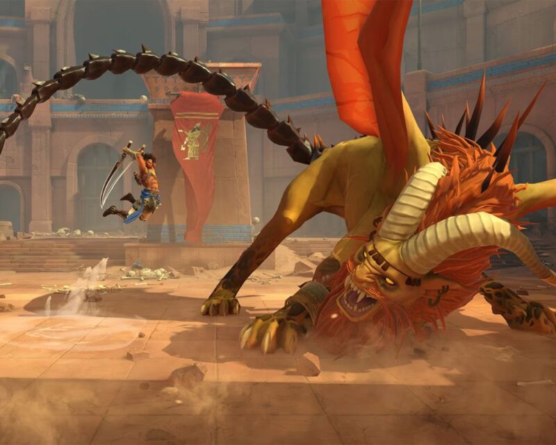 grafika z gry Prince of Persia: The Lost Crown, widzimy na niej głównego bohatera (mężczyznę bez koszulki, w niebieskich spodniach i z dużym mieczem) podczas skoku-ataku na mantykorę (rogatego potwora o kolorach pomarańczowo-żółtych ze skrzydłami i długim ogonem), dookoła widać arenę i piasek
