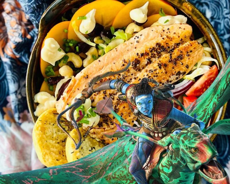 Avatar Frontiers of Pandora przepis sałatka, na zdjęciu widzimy sałatkę z grzankami, łososiem, owocami kaki i innymi składnikami; na zdjęcue sałatki nałożona jest grafika z postacią z gry Avatar Frontiers of Pandora