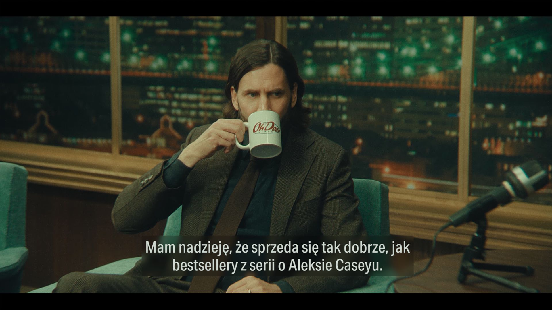 Obrazek przedstawia Alana Wake'a (Ilkka Villi). Otoczenie wskazuje na to, że jest gościem programu typu talk-show. Pije z kubka z napisem "Oh Deer Diner". Pod spodem widnieje fragment dialogu: "Mam nadzieję, że sprzeda się tak dobrze, jak bestsellery z serii o Aleksie Caseyu".