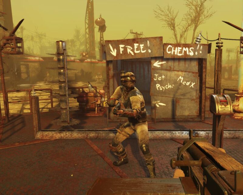 Postać z gry Fallout, ubrana w strój ochronny. Trzyma broń. Za nią stoi budka z napisem "darmowe chemikalia". W tle widać zniszczone budynki.