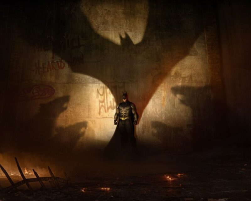 Batman stoi pod ścianą, w tle widać jego symbol