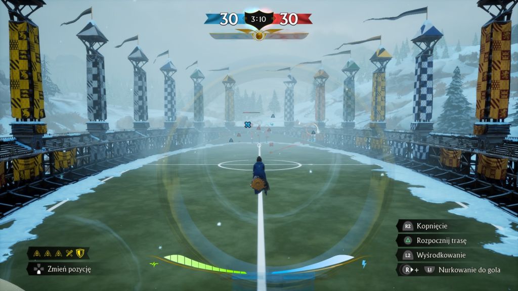 Obrońca na miotle pilnuje, by nikt nie strzelił gola przez jedną z obręczy. Widać zaśnieżone boisko, wieżyczki z flagami, interfejs gry: wynik meczu, pozycja i działania gracza.