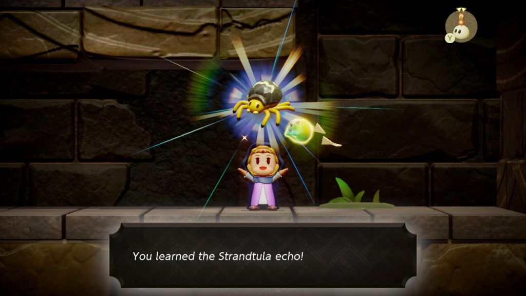 Bohaterka jest w podziemiach, przytrzymuje pająka, wokół ciemne barwy. 