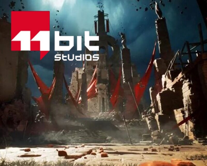 Logo studia 11 bit studios na tle zrujnowanej, postapokaliptycznej lokacji z monumentalnymi filarami, czerwonymi sztandarami i dramatycznym, ciemnym niebem.