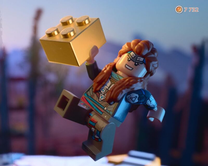 Screen z gry LEGO Horizon Adventures z główną bohaterką, Aloy, i złotym klockiem lego na pierwszym planie.