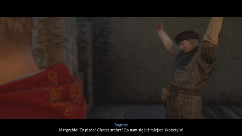 Po prawej mężczyzna w skromnym odzieniu podnosi ręce, w tle kamienne mury twierdzy. Po lewej kawałek szyi jego towarzysza w czerwonym ubraniu,