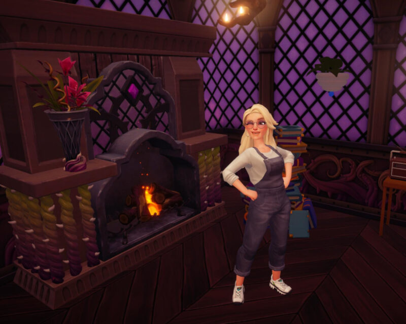 Na obrazku znajduje się postać z gry Disney Dreamlight Valley. Ma blond włosy, szare ogrodniczki i białe buty sportowe. Ma pozę z rękoma na biodrach i puszcza oczko. Za nią znajduje się wielki kominek w gotyckim klimacie. Pali się w nim ogień. Ściany w domu są ciemno-fioletowe. Cały obrazek jest w ciemnej kolorystyce.