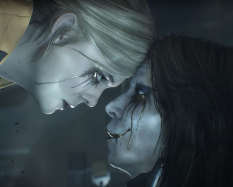 Na obrazku znajdują się dwie postaci z gry Death Stranding 2: On The Beach. Obydwie osoby mają szarą skórę i czarne, rozmazane makijaże. Jedna z postaci ma blond włosy, a druga czarne włosy. Stykają się czołami i patrzą na siebie.