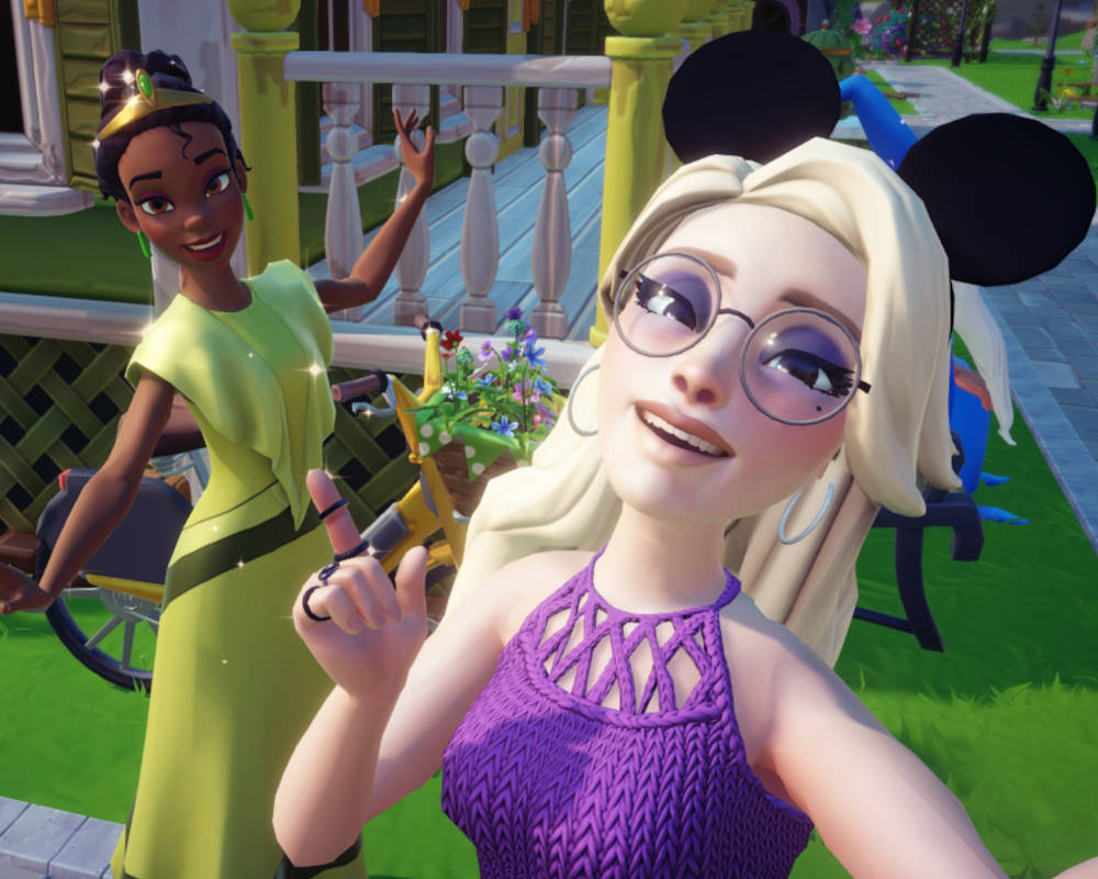 Na tym obrazku widzimy scenę z gry wideo „Disney Dreamlight Valley”. Sceneria jest bajkowa, z kolorowymi budynkami i dekoracjami. Na pierwszym planie stoi postać gracza, mająca na sobie koszulę w kwiaty, jeansowe szorty i białe trampki. Postać ma jasno niebieskie włosy. Wokół postaci znajdują się różne budynki i dekoracje, które nadają miejscu klimat miasteczka Disneya. Widać różne małe domki i dekoracje kwiatowe. Wszędzie rosną drzewa. Grafika jest trójwymiarowa, kolorowa i stylizowana na animacje Disneya. Gra posiada bardzo przyjemny, kreskówkowy styl. Obrazek emanuje radosną i bajkową atmosferą, typową dla produkcji Disneya.