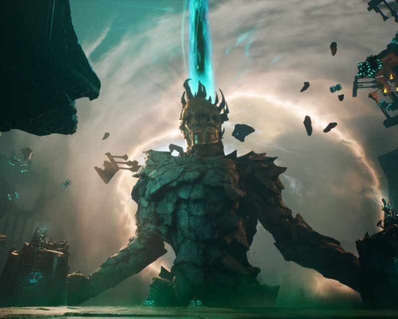 Na obrazku widać ogromnego, kamiennego giganta z złotą maską na twarzy, otoczonego mrocznym krajobrazem. W tle unosi się tajemniczy wir energii, a wokół latają fragmenty skał i konstrukcji.