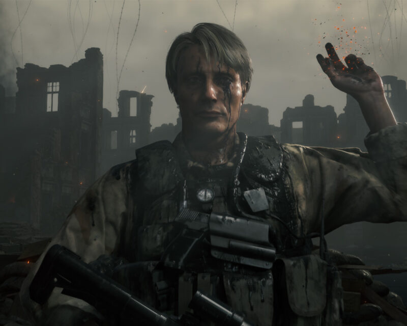 Mads Mikkelsen jako Cliff w grze Death Stranding, w mundurze na tle zniszczonego miasta.