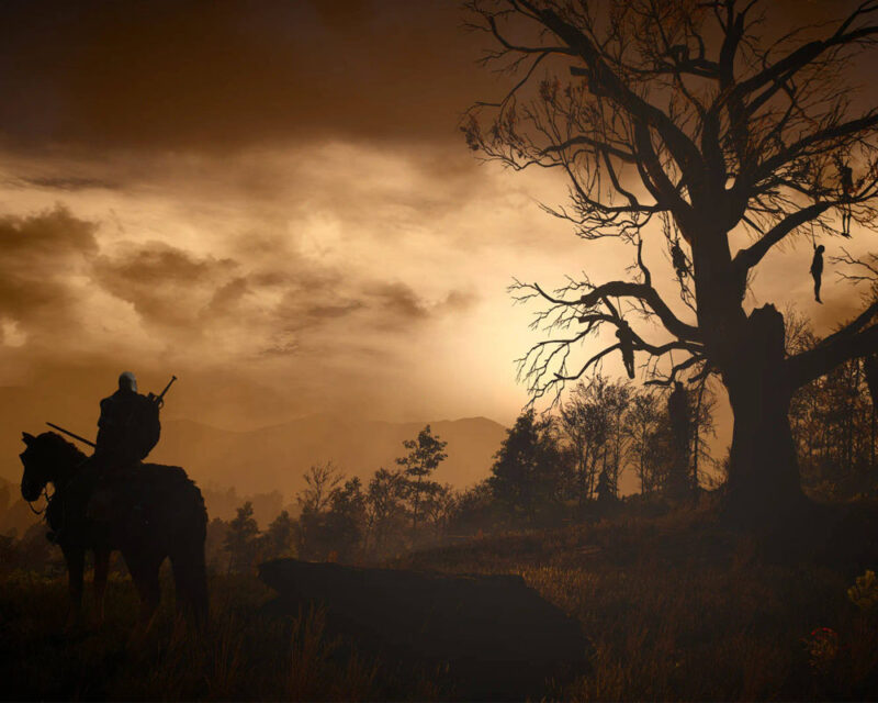 Grafika przedstawia rozłożysty dąb z gry Wiedźmin 3 Dziki Gon o nazwie Drzewo Wisielców na tle ciemnego, zachmurzonego nieba. Obok widać jeźdźca na koniu.