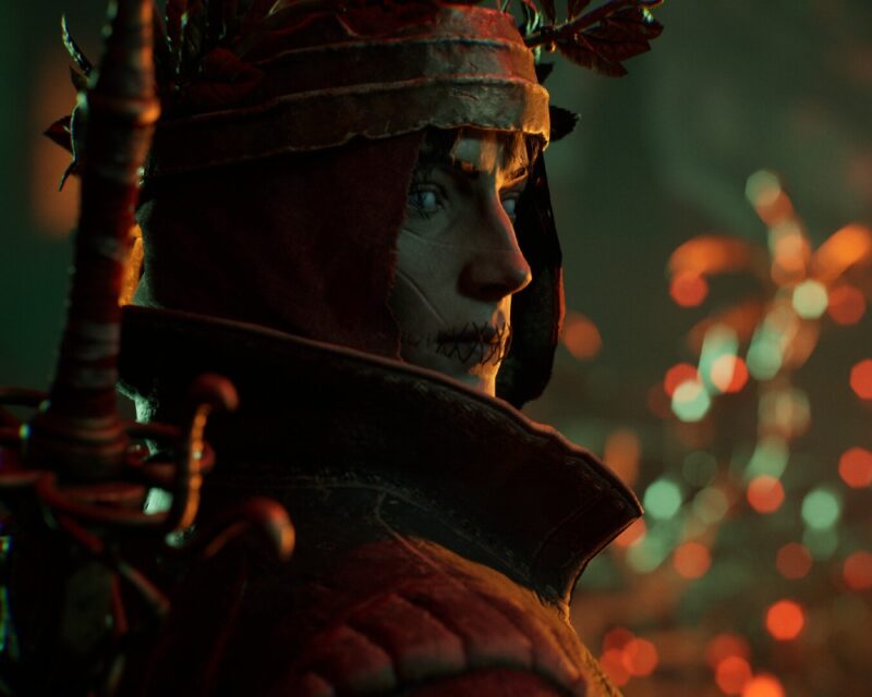 Zwiastun La Divina Commedia z Opening Night Live na Gamescomie - niepokojąca postać z zaszytymi ustami i w zbroi patrzy w kamerę, ograna trochę z boki , kadr z gry