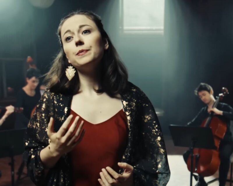 Na obrazku znajduje się Alice Duport-Percier podczas wykonywania piosenki. Ma skupioną twarz. Jest ubrana w czerwoną sukienkę i ma czarno-złotą narzutę. Ma złote kolczyki. Kobieta ma ciemne włosy do ramion. Za nią widać muzyka, który gra na wiolonczeli.