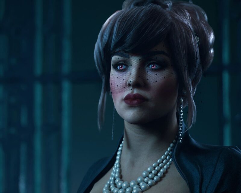 grafika z gry Vampire: The Masquerade – Bloodlines 2, przedstawia jedną z postaci z gry, bladą kobietę z czarnymi, spiętymi u góry włosami i z czarnym woalem okalającym górną połowę twarzy, ma różowe policzki i krwistoczerwone usta, na szyi wisi duży naszyjnik z pereł, za nią widzimy fragment budynku