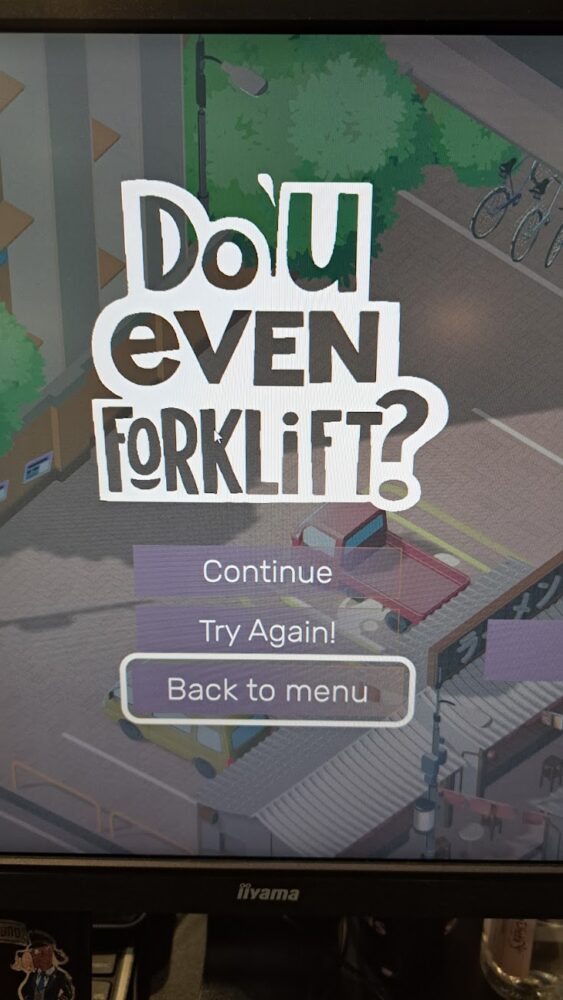 Monitor wyświetlający menu gry pt. "Do you even forklift?", pod napisami widać samochody na parkingu.