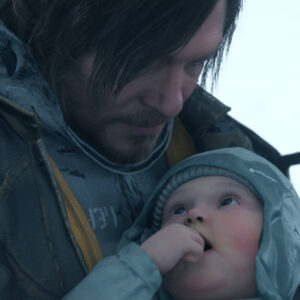 Na zbliżeniu widać Sama Portera Bridgesa (postać z gry Death Stranding, graną przez Normana Reedusa) trzymającego BB (Bridge Baby). Sam ma długie, ciemne włosy i patrzy na dziecko z łagodnym wyrazem twarzy. Jest ubrany w techniczny strój kuriera z żółtymi akcentami. Dziecko ma na sobie niebieską czapkę i kaptur, patrzy w górę, a jego rączka znajduje się przy ustach. Scena ma chłodną, szarobłękitną kolorystykę, sugerującą, że akcja dzieje się na zewnątrz.