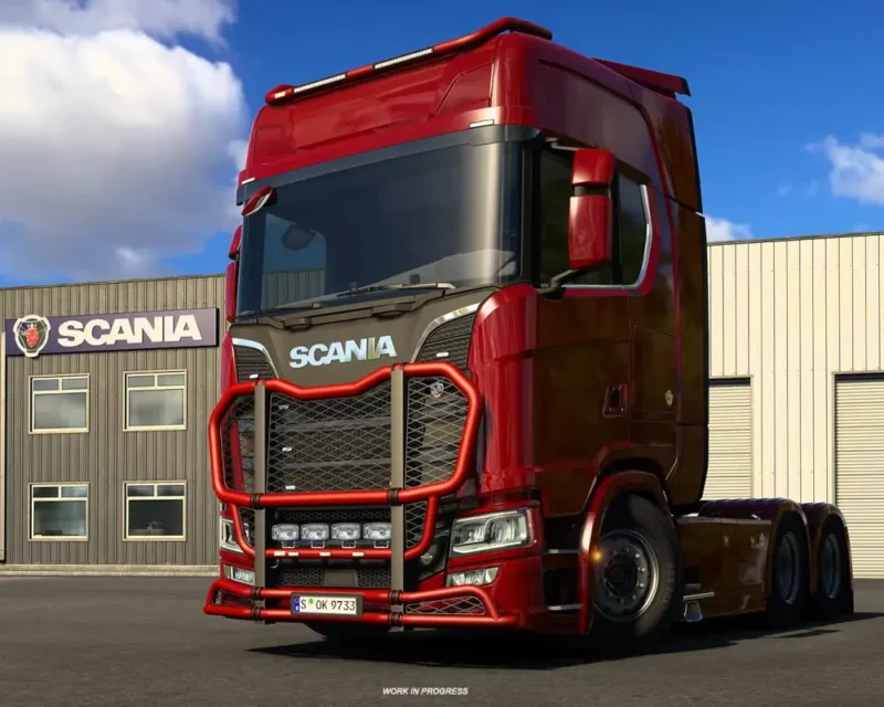Na ilustracji z gry **Euro Truck Simulator 2** widać czerwoną ciężarówkę marki Scania zaparkowaną przed budynkiem serwisowym z logo producenta. Pojazd ma masywny zderzak ochronny i charakterystyczne detale karoserii, a w tle widać niebo z lekkim zachmurzeniem.