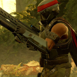 Na obrazku widać postać w zbroi i hełmie, która trzyma w rękach duży karabin lub strzelbę z podwójnymi lufami. Postać ma na sobie ciemnozielony lub czarny pancerz z czerwoną opaską/bandaną zawiązaną na czole pod hełmem oraz czerwoną pelerynę zarzuconą na ramiona. Ubiór i opaska nawiązują stylem do postaci Johna Rambo. Scena rozgrywa się w lesistym lub dżunglowym otoczeniu, z gęstą roślinnością i zamglonym, jasnym tłem, co sugeruje, że jest to kadr z gry wideo Helldivers 2. Postać jest skierowana w prawą stronę, w pozycji bojowej.