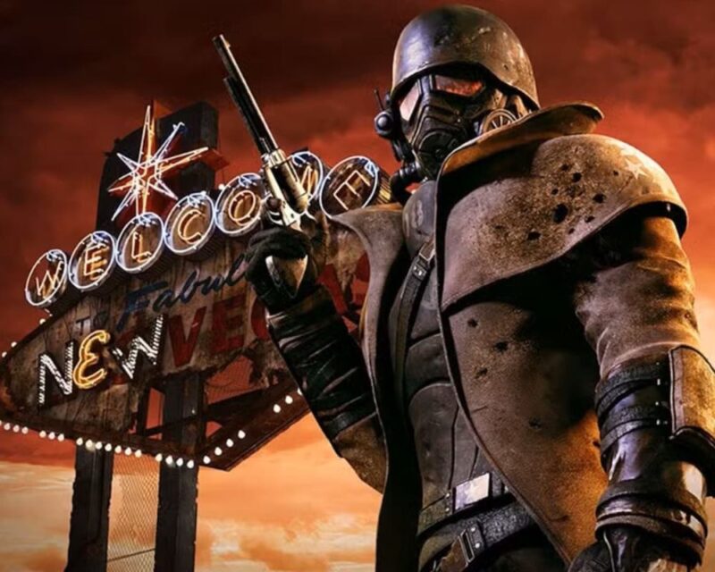 Postać NCR Rangera z gry Fallout: New Vegas w charakterystycznym pancerzu bojowym i masce przeciwgazowej trzyma rewolwer, stojąc na pierwszym planie. W tle widoczny jest podświetlony neon „Welcome to Fabulous New Vegas” oraz pustynny krajobraz skąpany w czerwono-pomarańczowym świetle zachodzącego słońca, podkreślający postapokaliptyczny klimat gry.