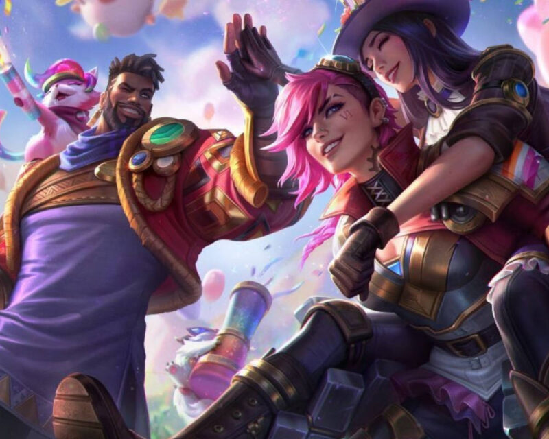 Obrazek przedstawia kolorową, dynamiczną ilustrację z gry League of Legends, utrzymaną w radosnym i uroczystym klimacie. Na pierwszym planie widać postać Vi o charakterystycznych różowych włosach, która uśmiecha się pewnie siebie, oraz Caitlyn, która przytula się do niej z zamkniętymi oczami. Obok nich stoi uśmiechnięty K'Sante w stroju z fioletowymi i złotymi akcentami, a w tle pojawia się radosny kot Yuumi oraz motywy konfetti i balonów, co sugeruje atmosferę świętowania lub specjalnego wydarzenia w świecie gry.