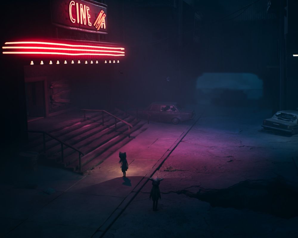 Ciemna, nocna ulica z opuszczonym kinem oznaczonym neonowym napisem „CINE”. Różowo-czerwone światło z szyldu oświetla schody prowadzące do wejścia oraz fragment pustej ulicy. Na pierwszym planie stoją dwie małe postacie w płaszczach z kapturami, patrzące w stronę budynku. W tle widać zaparkowane samochody i zarys wysokich, ponurych budynków, a cała scena ma tajemniczy, niepokojący klimat.
