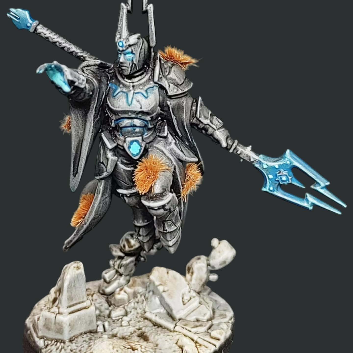 Figurka Knight-Arcanum – Stormcast Eternal w motywie ożywionego posągu Zdjęcie pomalowanej figurki fantasy przedstawiającej zakutego w pełną zbroję płytową wojownika-maga w dynamicznej, lewitującej pozie. Pancerz ma kolor jasnego, spatynowanego kamienia lub marmuru z wyraźnym cieniowaniem. Spod hełmu, z dłoni oraz z nacięć na napierśniku bije jasnoniebieska poświata, sugerująca magiczną energię. Postać dzierży kostur zakończony trójzębnym grotem w tym samym błękitnym kolorze. Na zbroi widoczne są kępki pomarańczowego mchu lub porostów, co nadaje figurce antyczny wygląd. Wojownik unosi się nad podstawką imitującą zrujnowane, kamienne sanktuarium.